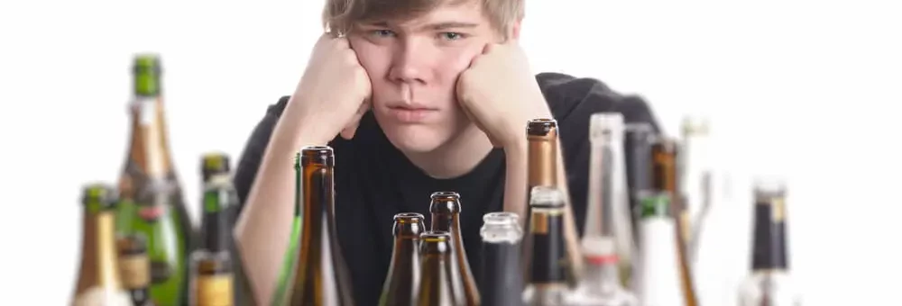 A man is pouting in front of a table filled with alcoholic bottles.