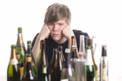 A man is pouting in front of a table filled with alcoholic bottles.