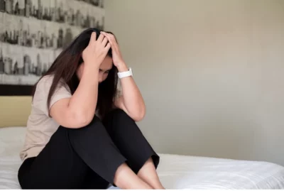 Distressed woman sits on bed with head in her hands