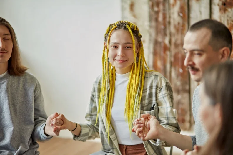 Young woman smiles and holds hands with others in an IOP group therapy session