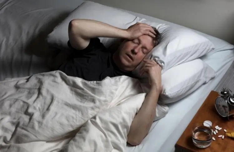 Distraught man holds head in bed with pile of fentanyl pills on bed stand