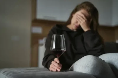 Woman with hand over her face holds a glass of wine