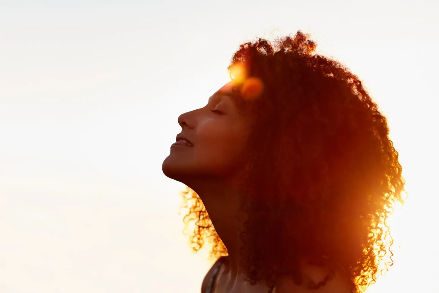 Sunlit silhouette of a hopeful woman with closed eyes