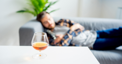 A man sleeping on a couch with a drink in the foreground.