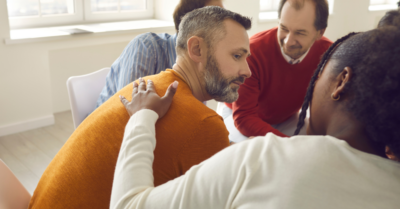 Main in an orange shirt being consoled in therapy