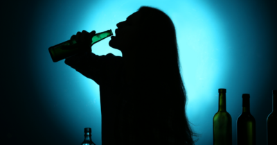 Shadowed silhouette of a woman drinking from a glass bottle.